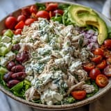A vibrant bowl of Tzatziki Chicken Salad with diced cucumber, red onion, and cherry tomatoes on a wooden table.