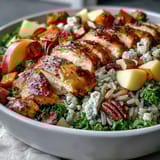 A vibrant Harvest Bowl with roasted sweet potatoes, kale, wild rice, tender chicken, apples, almonds, and goat cheese with balsamic dressing.  