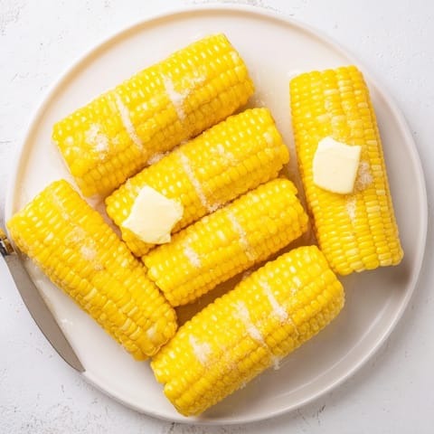 Freshly boiled sweet corn on the cob glistening with melted butter and a sprinkle of sea salt, served warm on a wooden board.