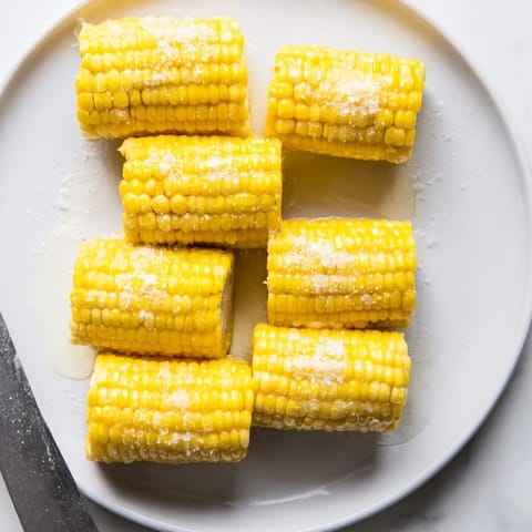 Golden grilled corn on the cob with charred kernels, brushed with creamy butter and dusted with salt, ready to enjoy outdoors.