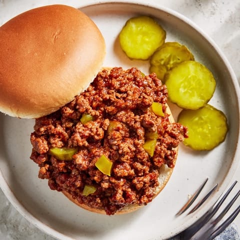 Savory Sloppy Joes simmered in tangy tomato sauce, served open-faced on a soft toasted bun with pickles.