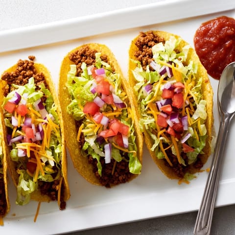 An overhead view of crunchy American-Style Tacos stuffed with juicy beef, lettuce, and a dollop of salsa.