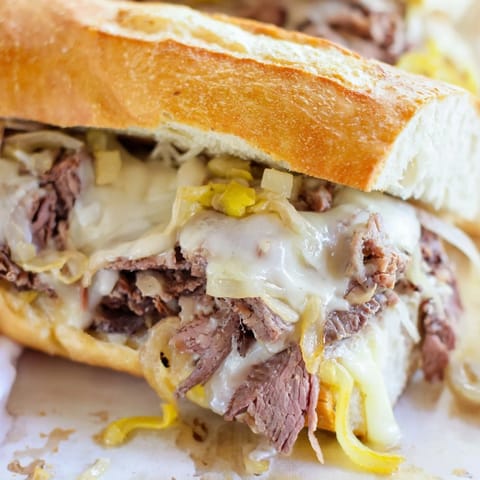 A close-up view of a hearty, messy Philly Cheesesteak sandwich stuffed with juicy steak, peppers, and gooey melted cheese.