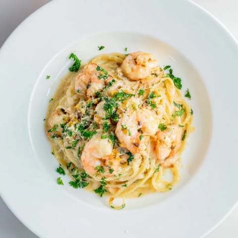 Creamy Garlic Shrimp Pasta is served on a white plate, featuring pink shrimp and golden linguine coated in a glossy, rich garlic cream sauce.