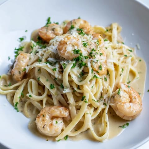 Twirls of al dente linguine in Creamy Garlic Shrimp Pasta are topped with parsley and lemon wedges, ready to be drizzled with sauce.