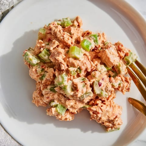 A close-up view of homemade Spicy Zesty Tuna Salad garnished with chopped scallions and parsley, ready to be piled high on toasted whole-grain bread.