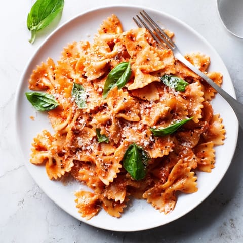 Creamy tomato basil bowtie pasta served hot with melted Parmesan and fresh basil garnish on a rustic plate.