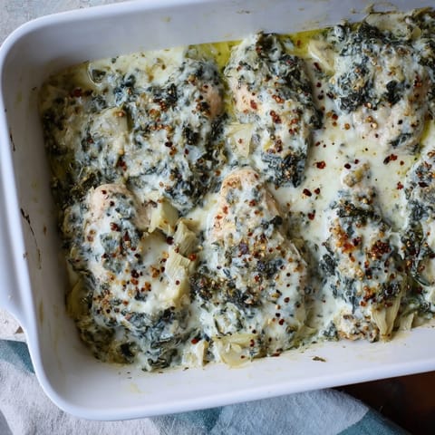 Juicy baked chicken breasts smothered in a creamy spinach and artichoke mixture, garnished with fresh parsley for a weeknight dinner.  