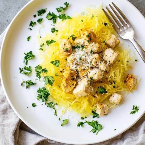 Tender lemon garlic chicken sautéed in olive oil is spooned over strands of roasted spaghetti squash, garnished with fresh parsley and grated Parmesan for a bright, healthy meal.  