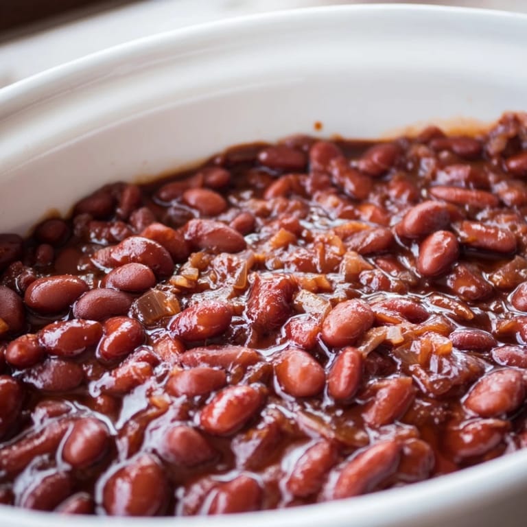 Hearty baked beans scooped from an ovenproof casserole, ready to serve as a savory vegetarian side dish.