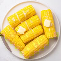 Freshly boiled sweet corn on the cob glistening with melted butter and a sprinkle of sea salt, served warm on a wooden board.