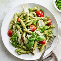 A close-up of vibrant Green Pesto Pasta Salad featuring fusilli pasta coated in basil pesto with cherry tomatoes and peas.  