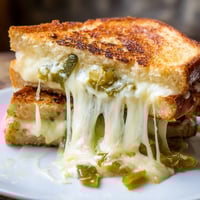 Golden-brown sourdough grilled cheese sandwich with melted pepper jack cheese and vibrant green pickled jalapeños on a rustic plate.